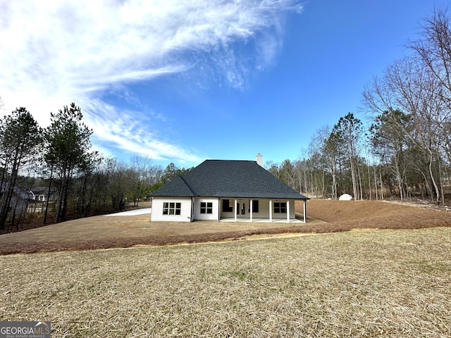 view of front facade with roof with shingles, a patio, and a chimney