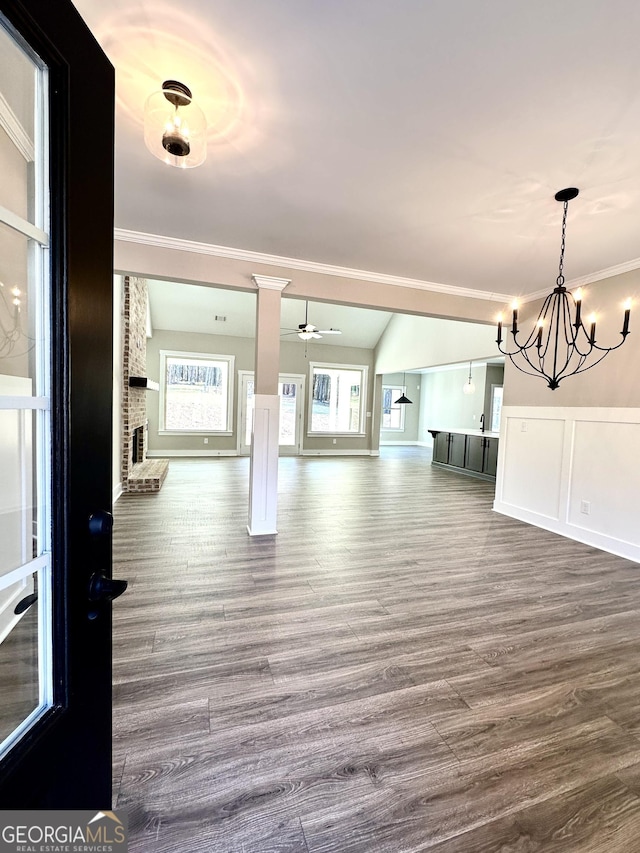 unfurnished living room with dark wood finished floors, crown molding, a fireplace, a decorative wall, and ceiling fan with notable chandelier