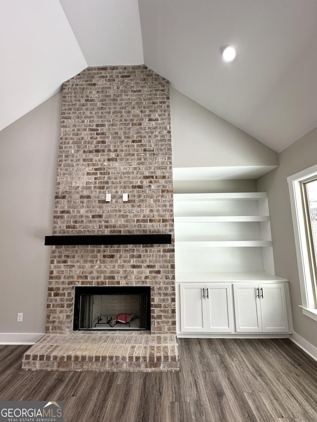 unfurnished living room with vaulted ceiling, a brick fireplace, wood finished floors, and baseboards