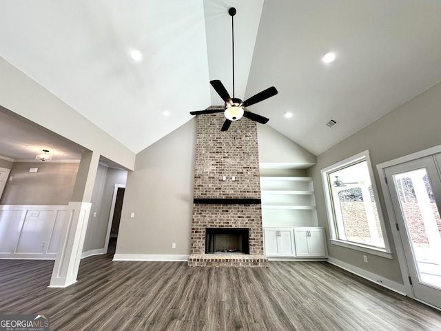 unfurnished living room featuring ceiling fan, visible vents, built in features, a brick fireplace, and dark wood finished floors