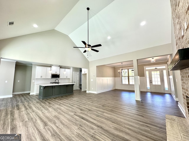 unfurnished living room with high vaulted ceiling, ceiling fan with notable chandelier, visible vents, and wood finished floors