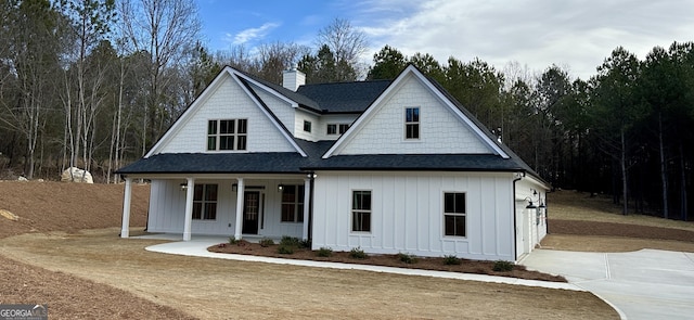 view of front of home featuring a chimney, a porch, board and batten siding, and a shingled roof