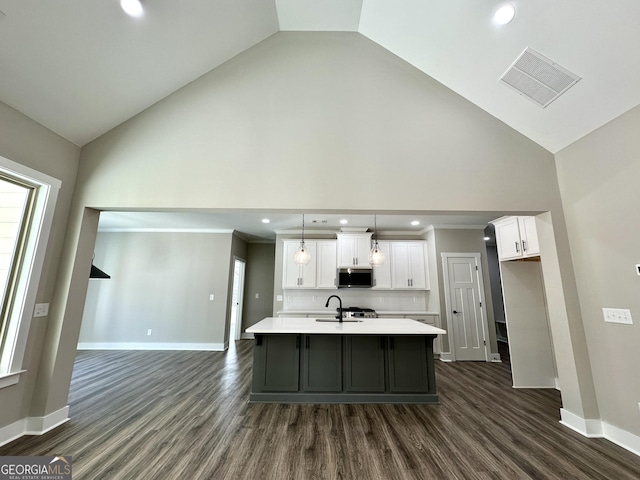 kitchen featuring visible vents, an island with sink, stainless steel microwave, light countertops, and white cabinetry