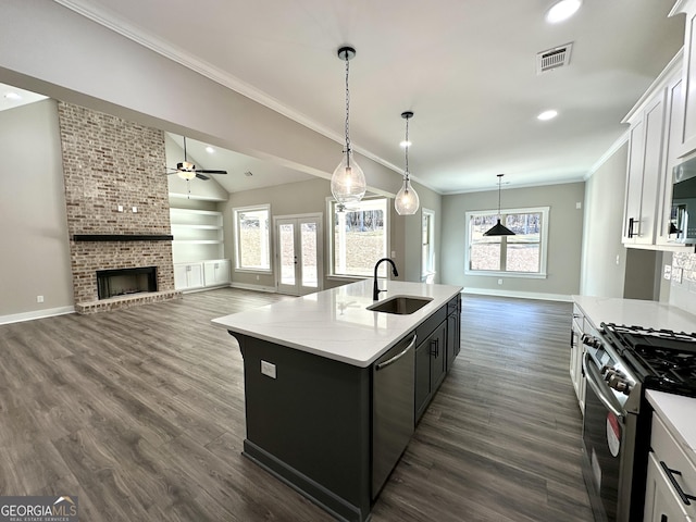 kitchen featuring visible vents, appliances with stainless steel finishes, ornamental molding, a kitchen island with sink, and a sink