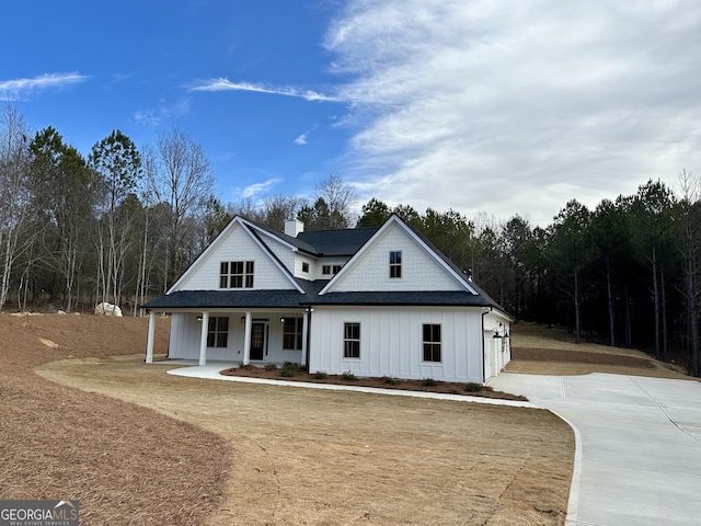 view of front of property featuring a chimney, a porch, board and batten siding, and roof with shingles