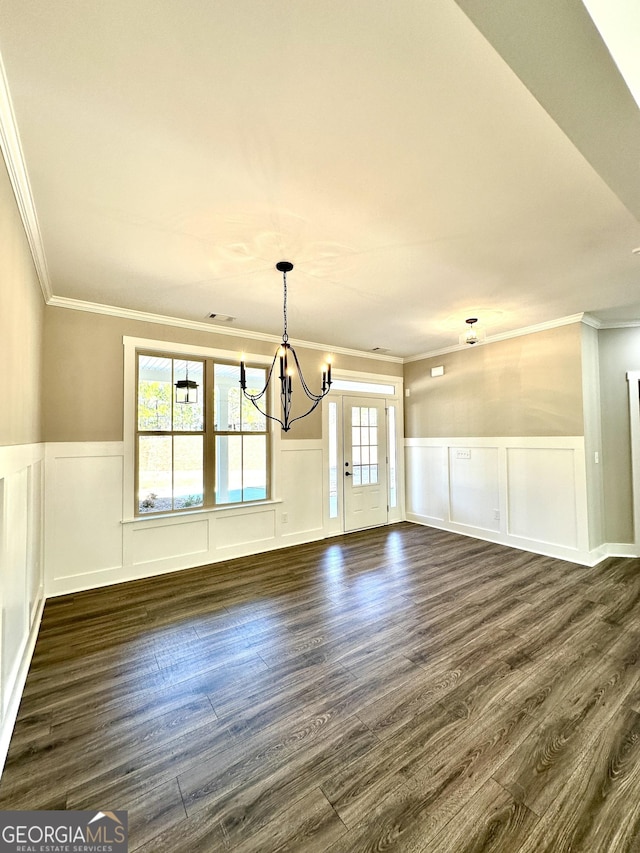 unfurnished dining area with an inviting chandelier, dark wood finished floors, crown molding, and a wainscoted wall