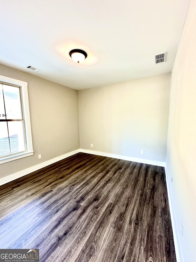 unfurnished room featuring dark wood-style flooring, visible vents, and baseboards