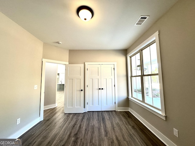 unfurnished bedroom with dark wood-type flooring, a closet, visible vents, and baseboards