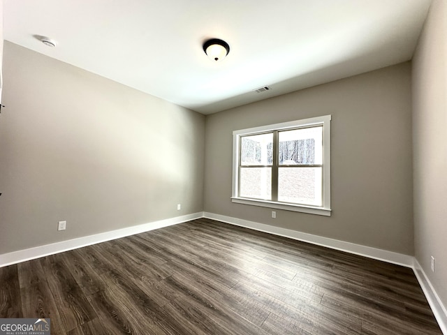 empty room with dark wood-style flooring, visible vents, and baseboards