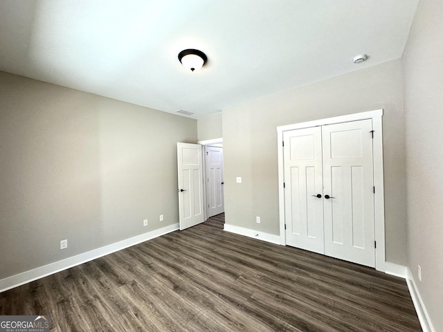 unfurnished bedroom featuring dark wood-style flooring, a closet, visible vents, and baseboards