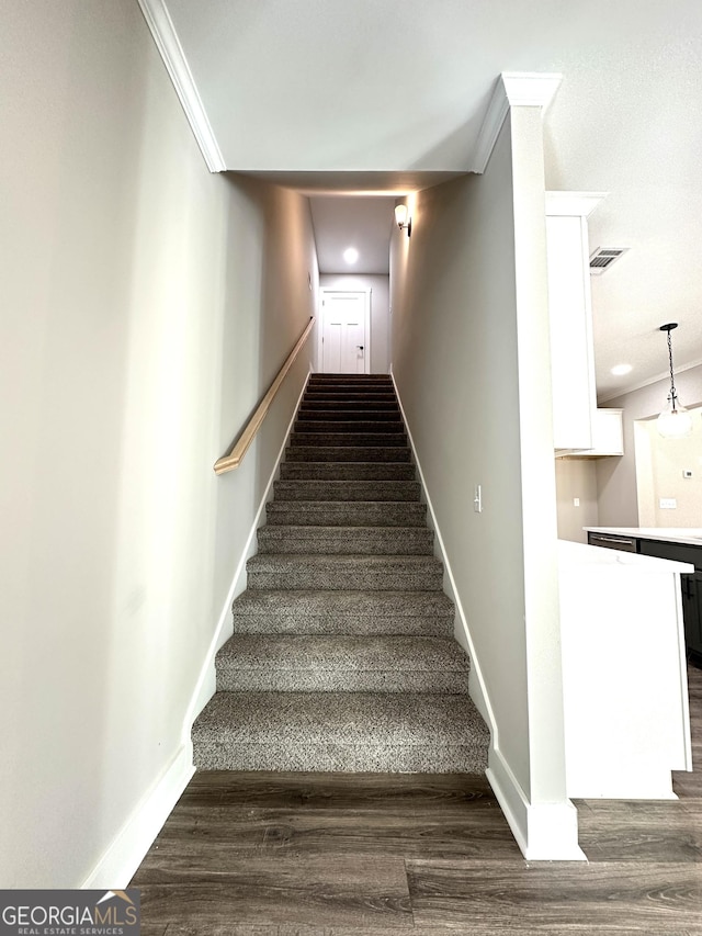 staircase featuring baseboards, wood finished floors, visible vents, and crown molding