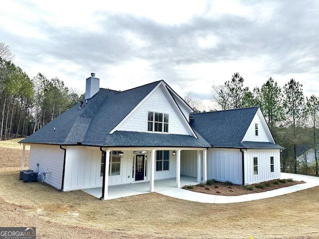 view of front facade with cooling unit, board and batten siding, and roof with shingles