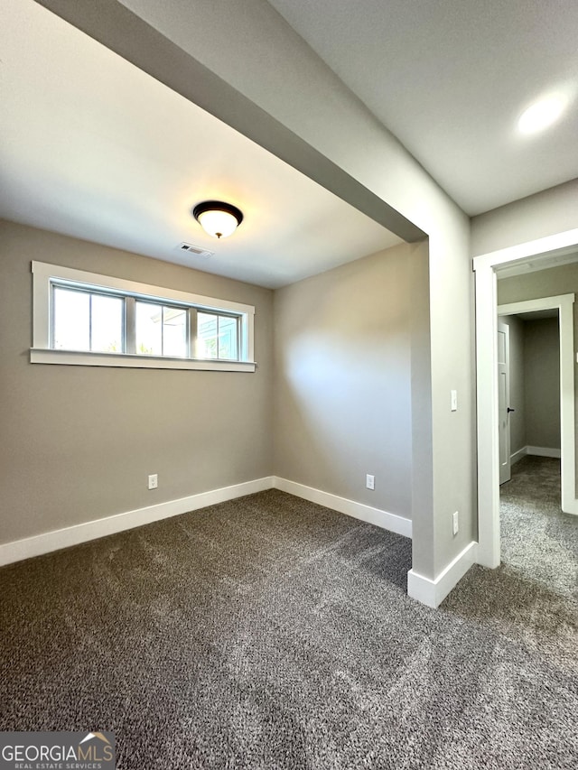 spare room featuring visible vents, dark carpet, and baseboards