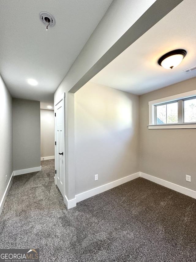 basement with baseboards, visible vents, and dark colored carpet