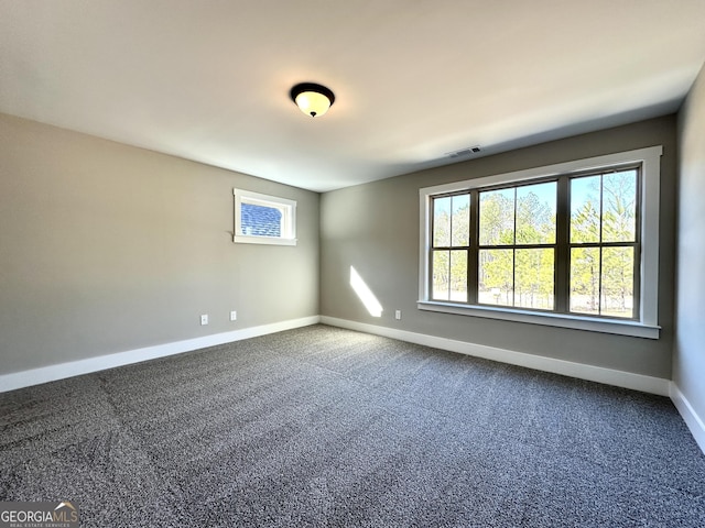 empty room with dark carpet, visible vents, and baseboards