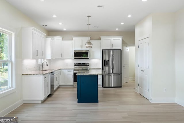 kitchen with pendant lighting, sink, light stone countertops, appliances with stainless steel finishes, and a kitchen island