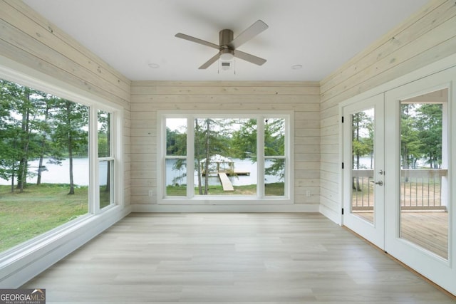 unfurnished sunroom featuring a water view, a wealth of natural light, french doors, and ceiling fan