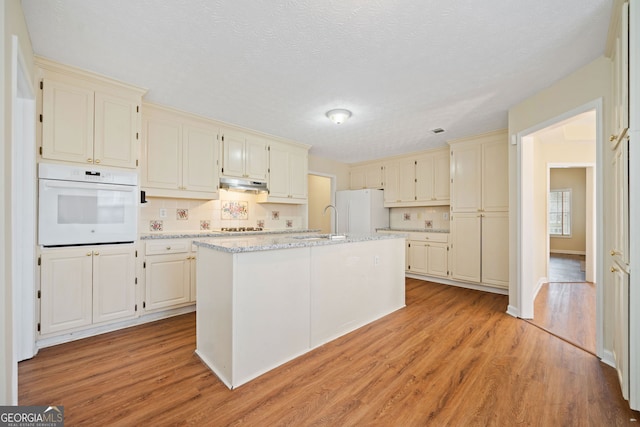 kitchen featuring white appliances, tasteful backsplash, light hardwood / wood-style flooring, and a center island with sink