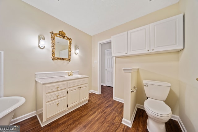 bathroom with a bath, vanity, wood-type flooring, and toilet