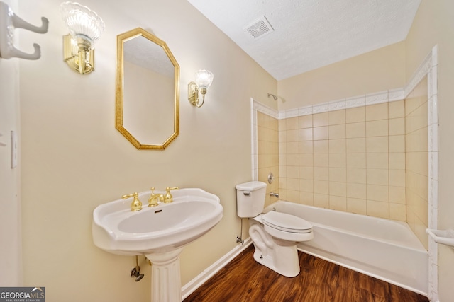 bathroom featuring hardwood / wood-style floors, tiled shower / bath combo, a textured ceiling, and toilet