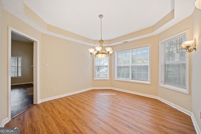 unfurnished dining area featuring hardwood / wood-style flooring, a raised ceiling, and a chandelier