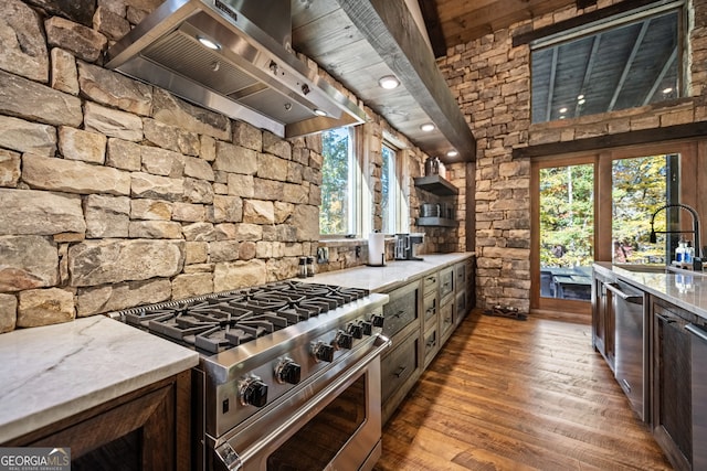 kitchen with light stone counters, stainless steel appliances, sink, wall chimney range hood, and hardwood / wood-style flooring