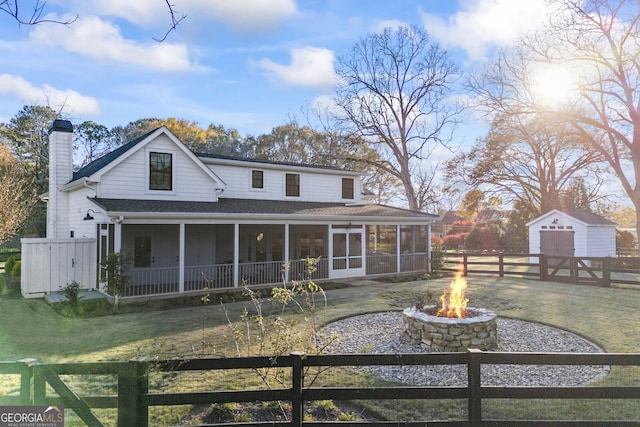 rear view of house with an outdoor fire pit, a storage shed, and a lawn