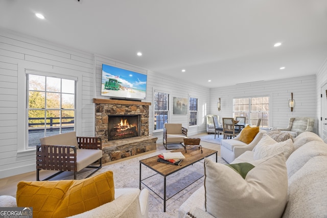 living room with light wood-type flooring, a stone fireplace, a healthy amount of sunlight, and wood walls