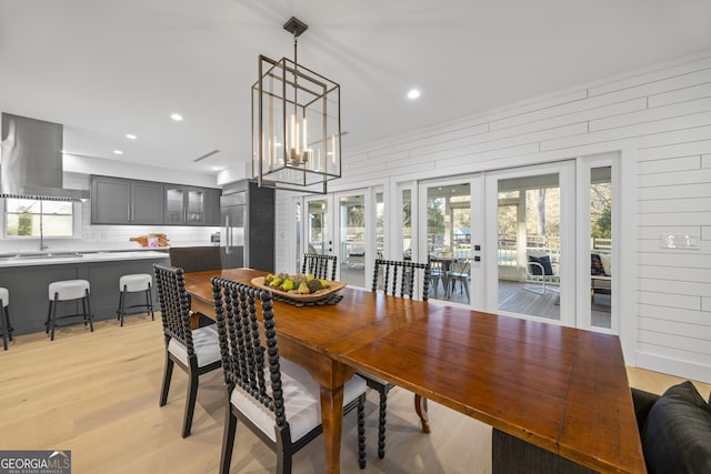 dining area with a healthy amount of sunlight, an inviting chandelier, light wood-type flooring, and french doors