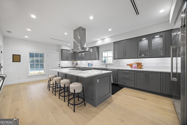 kitchen with light hardwood / wood-style floors, island range hood, a kitchen island, and a healthy amount of sunlight