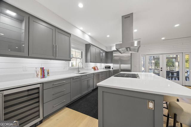 kitchen with a center island, sink, island exhaust hood, beverage cooler, and stainless steel appliances