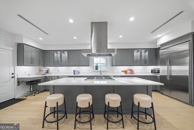 kitchen with a kitchen island, island exhaust hood, stainless steel appliances, and a breakfast bar area