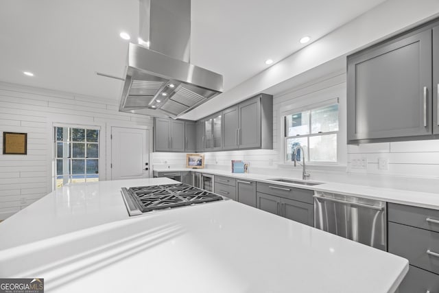 kitchen with sink, wooden walls, gray cabinets, island range hood, and appliances with stainless steel finishes