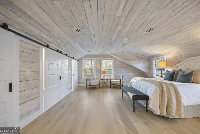 bedroom with vaulted ceiling, wooden walls, a barn door, wooden ceiling, and hardwood / wood-style floors