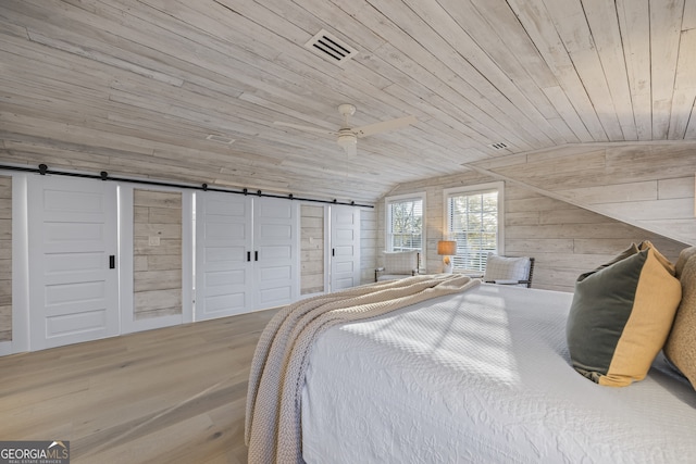 bedroom featuring a barn door, vaulted ceiling, wooden ceiling, and wood walls