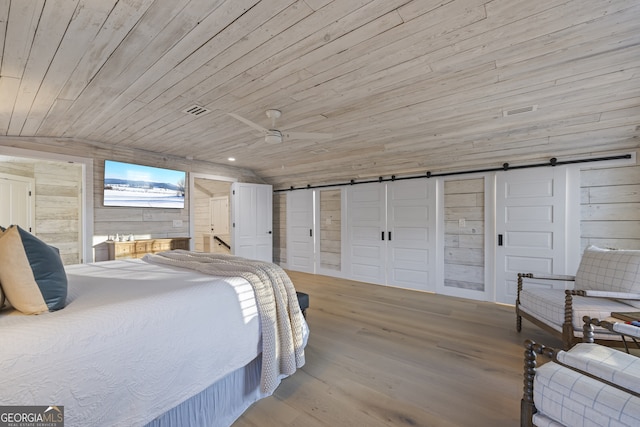 bedroom featuring vaulted ceiling, ceiling fan, wooden walls, a barn door, and light hardwood / wood-style flooring