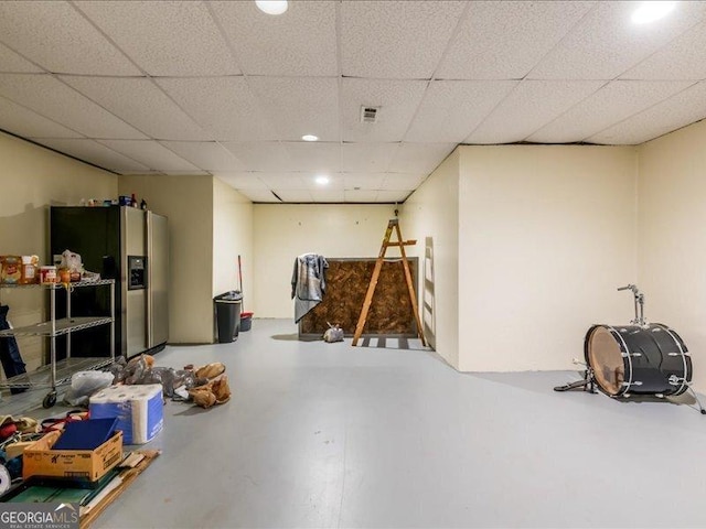 basement with a drop ceiling and stainless steel fridge