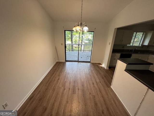 unfurnished dining area with a chandelier, sink, dark wood-type flooring, and vaulted ceiling