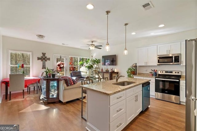 kitchen with an island with sink, stainless steel appliances, decorative light fixtures, white cabinets, and sink