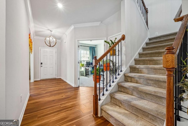 foyer entrance featuring wood-type flooring, ornamental molding, and a chandelier