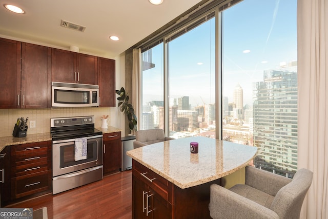 kitchen featuring dark hardwood / wood-style floors, light stone counters, backsplash, and appliances with stainless steel finishes