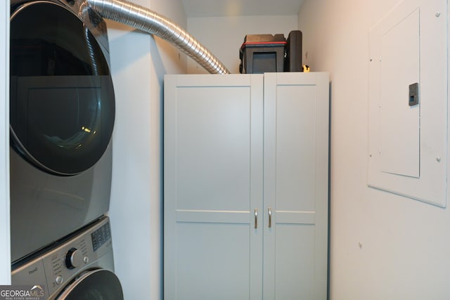 washroom with electric panel, cabinets, and stacked washer and clothes dryer