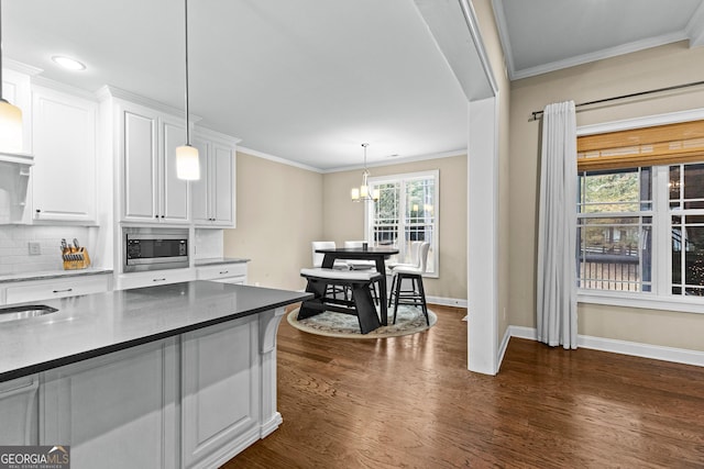 kitchen featuring dark hardwood / wood-style floors, stainless steel microwave, white cabinetry, and decorative light fixtures