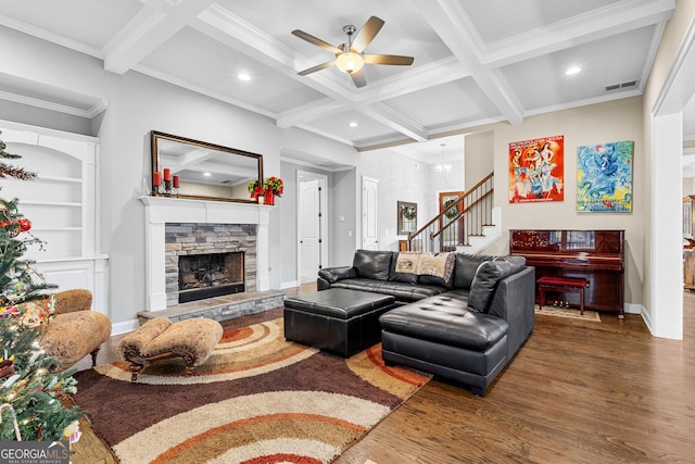 living room featuring coffered ceiling, a stone fireplace, hardwood / wood-style flooring, ornamental molding, and beamed ceiling