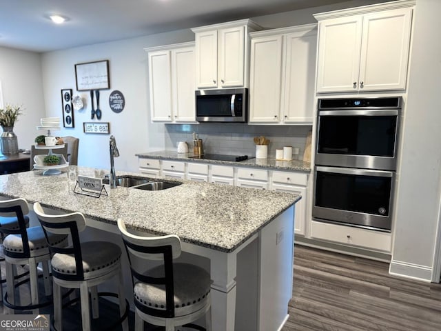 kitchen with white cabinetry, sink, dark wood-type flooring, stainless steel appliances, and an island with sink