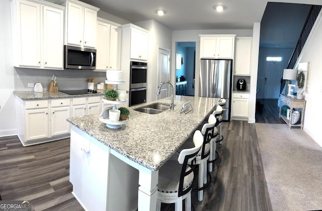 kitchen with a kitchen island with sink, sink, dark hardwood / wood-style flooring, light stone counters, and stainless steel appliances