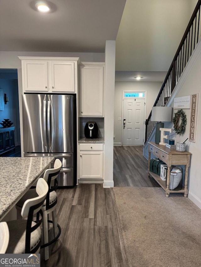 kitchen featuring white cabinets, dark hardwood / wood-style floors, stainless steel fridge, and light stone countertops