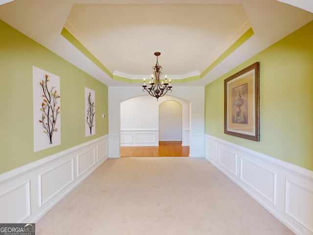 carpeted empty room with a tray ceiling, a notable chandelier, and ornamental molding