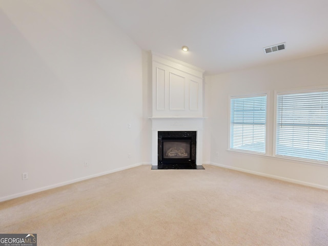 unfurnished living room featuring a high end fireplace and light colored carpet