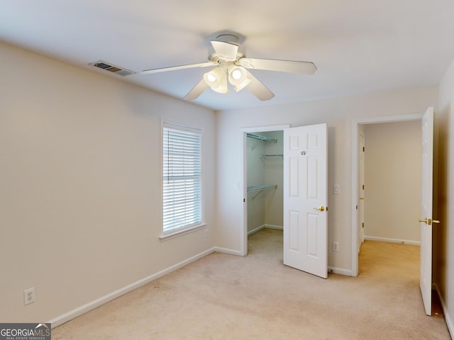 unfurnished bedroom featuring a closet, a walk in closet, light colored carpet, and ceiling fan